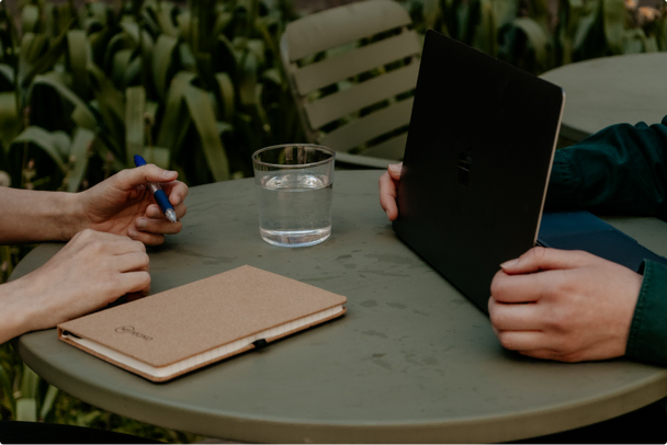 A Mono Solutions notebook on a table, a glass of water, and a person working at a laptop