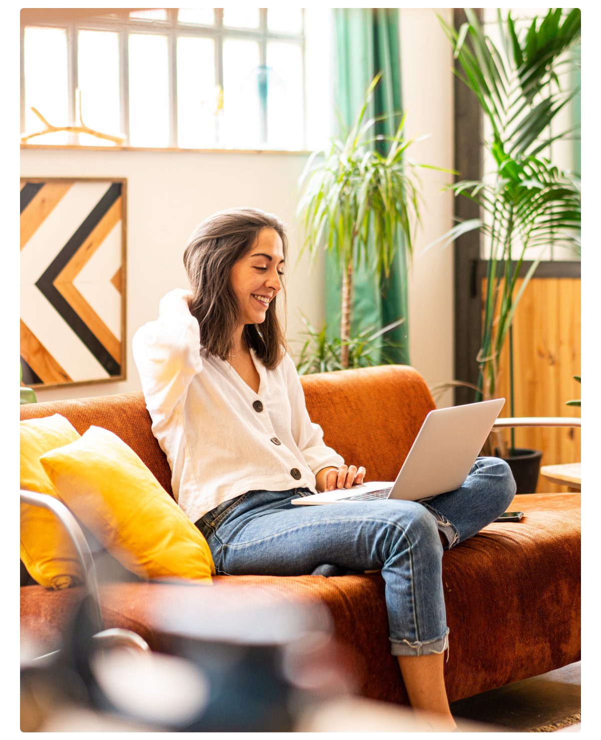 An image of a woman sitting on a couch while looking at the computer and smiling. 