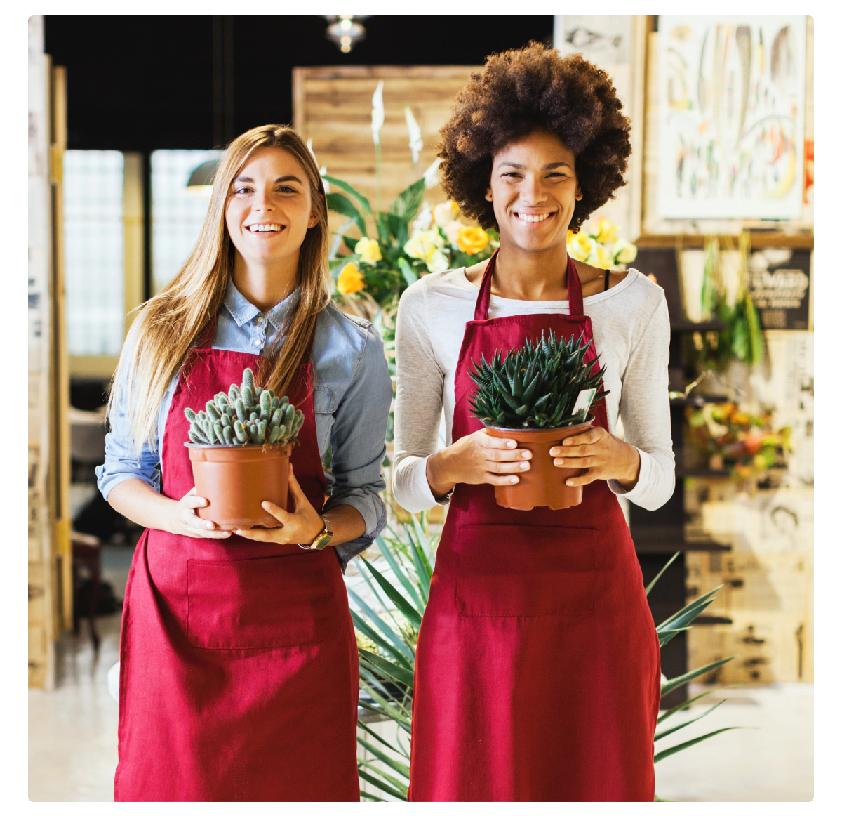 Image of two smiling employees holding plants in a flower shop. Meant to signify small business owners who are happy with the DIFM approach, as it gives them more time to spend working on aspects of the job they enjoy. 